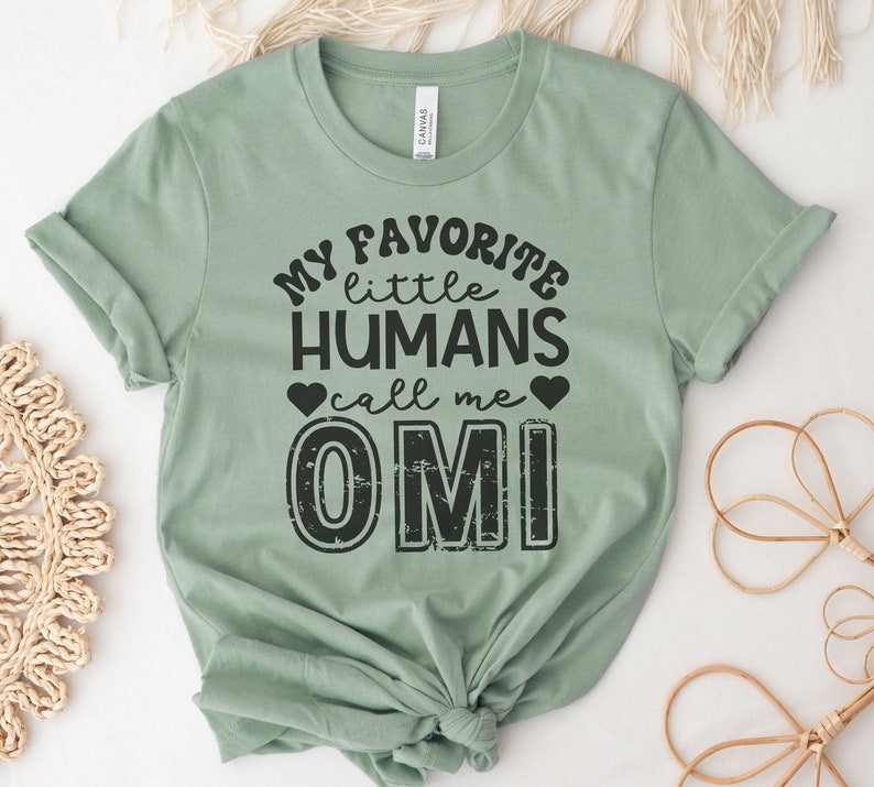 May include: A sage green t-shirt with black text that reads "My favorite little humans call me OMI".
