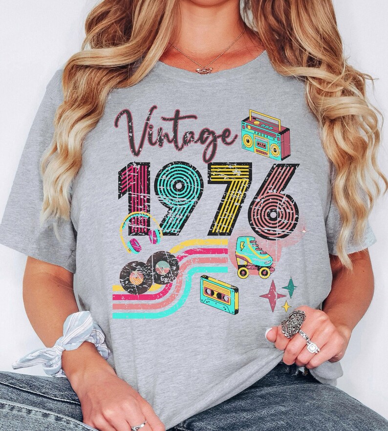 May include: A gray t-shirt with the text "Vintage 1976" in a retro design. The shirt features illustrations of a boombox, roller skate, cassette tape, and records, with colorful stripes and star accents.