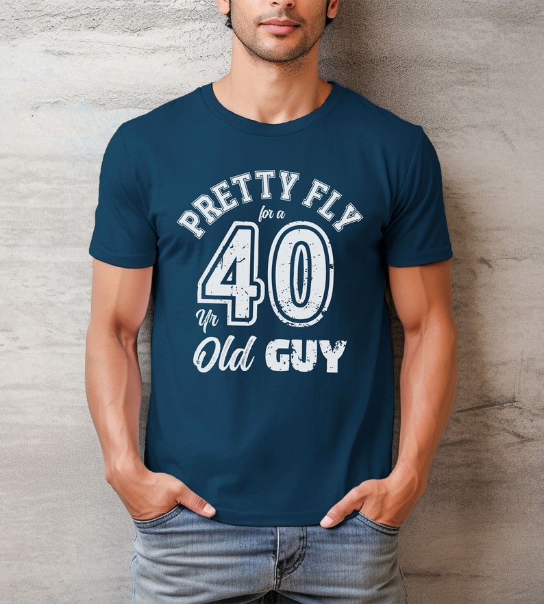 Pu&ograve; includere: Una t-shirt blu navy con una grafica bianca che dice "Pretty Fly for a 40 Yr Old Guy".