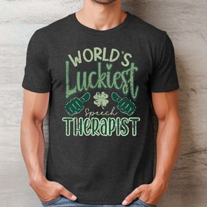 May include: Dark gray t-shirt with the text "WORLD'S Luckiest Speech Therapist" in green and white. The design includes a shamrock and thumbs-up graphics, perfect for speech therapists.