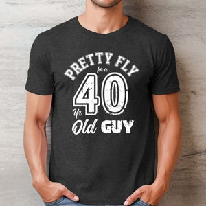 Pu&ograve; includere: Una t-shirt grigio scuro melange con una grafica bianca che dice "Pretty Fly for a 40 Yr Old Guy".