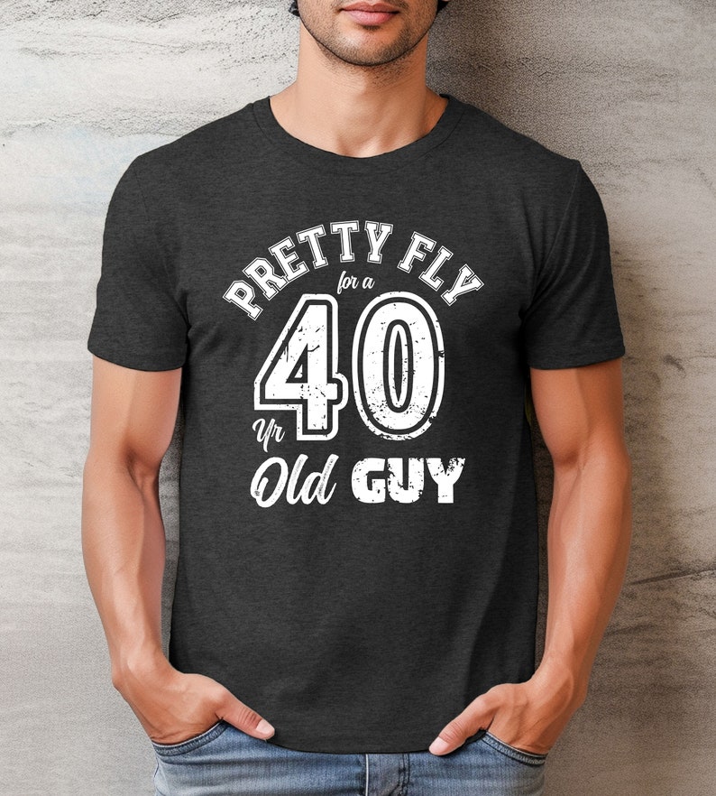 Pu&ograve; includere: Una t-shirt grigio scuro melange con una grafica bianca che dice "Pretty Fly for a 40 Yr Old Guy".