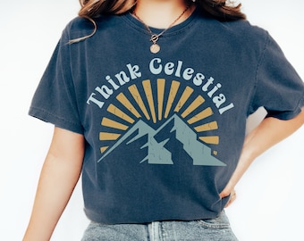 May include: Dark blue t-shirt with the text "Think Celestial" in a circular design above a mountain graphic. The graphic features a sunburst design in gold and a mountain range in blue and green.