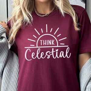 May include: A maroon t-shirt with a white graphic design of a sun with the text "Think Celestial" underneath.