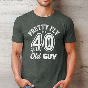 Pu&ograve; includere: Una maglietta verde scuro con una grafica bianca che dice "Pretty Fly for a 40 yr Old Guy".