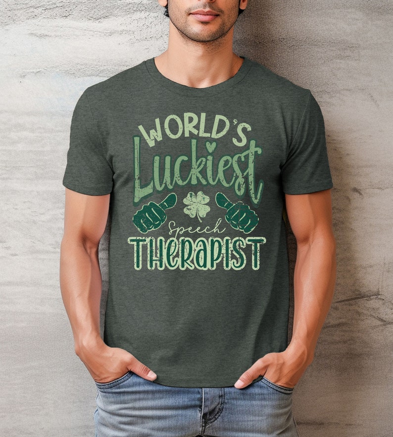 May include: Dark gray t-shirt with the text "WORLD'S Luckiest Speech Therapist" in green. The design includes a four-leaf clover and thumbs-up symbols. The shirt is made of a soft material and has a crew neck.