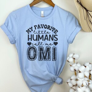 May include: Light blue t-shirt with black text that reads "My favorite little humans call me Omi".