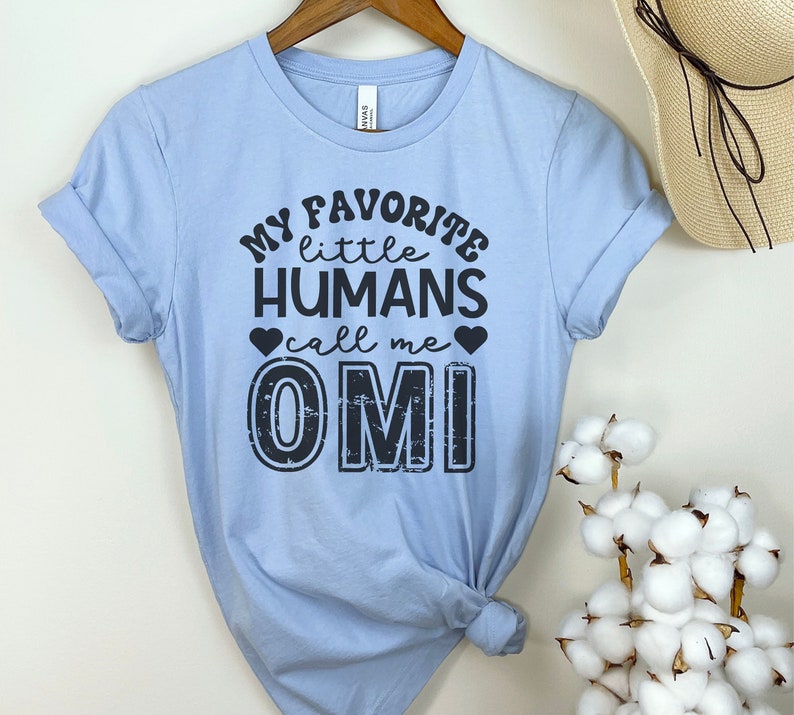 May include: Light blue t-shirt with black text that reads "My favorite little humans call me Omi".