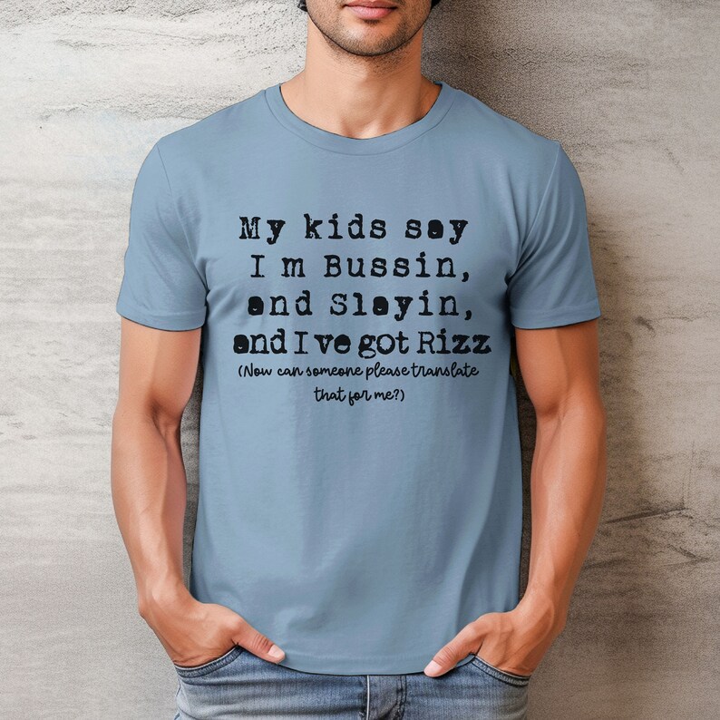 May include: A light blue t-shirt with black text. The text reads "My kids say I'm Bussin, and Slayin, and I've got Rizz. (Now can someone please translate that for me?)"