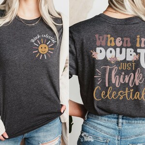 Puede incluir: Una camiseta gris oscuro con un gr&aacute;fico de sol y el texto "Think Celestial" en la parte delantera. La parte posterior de la camiseta tiene el texto "When in doubt, just think celestial!" con acentos florales.