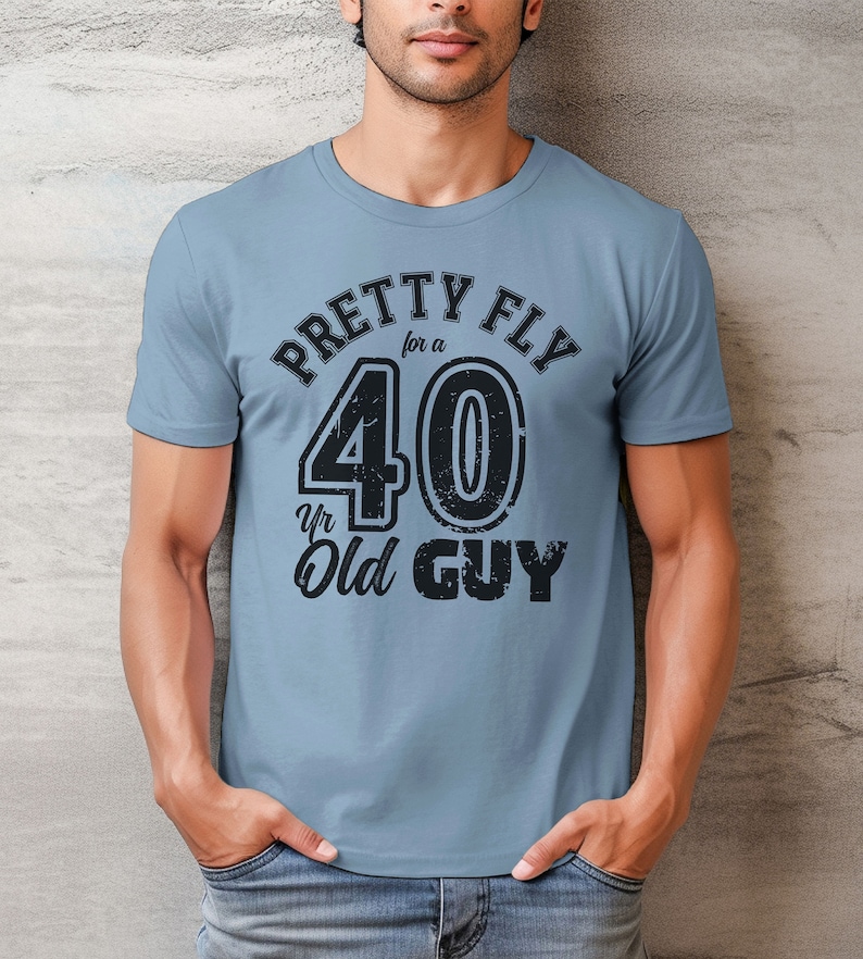 Pu&ograve; includere: Una maglietta blu con una grafica nera che dice "Pretty Fly for a 40 Yr Old Guy".
