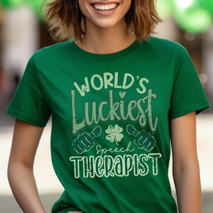 May include: A green t-shirt with the text "WORLD'S Luckiest Speech Therapist" in a distressed font. The design includes a four-leaf clover and thumbs-up symbols. The shirt is a solid green color.