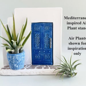 Pode incluir: Uma estrutura de parede branca em degraus com uma porta azul central com entalhes ornamentados e um puxador prateado. Um vaso azul texturizado cont&eacute;m uma planta a&eacute;rea, e uma segunda planta a&eacute;rea repousa na base. Texto: Mediterranean inspired Air Plant stand. Air Plants shown for inspiration only.