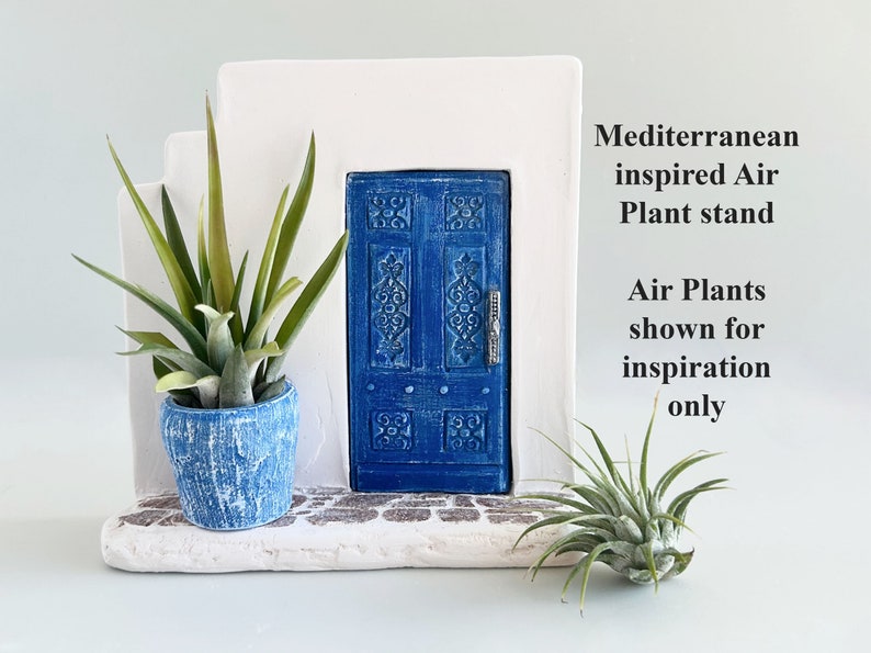 Pode incluir: Uma estrutura de parede branca em degraus com uma porta azul central com entalhes ornamentados e um puxador prateado. Um vaso azul texturizado cont&eacute;m uma planta a&eacute;rea, e uma segunda planta a&eacute;rea repousa na base. Texto: Mediterranean inspired Air Plant stand. Air Plants shown for inspiration only.