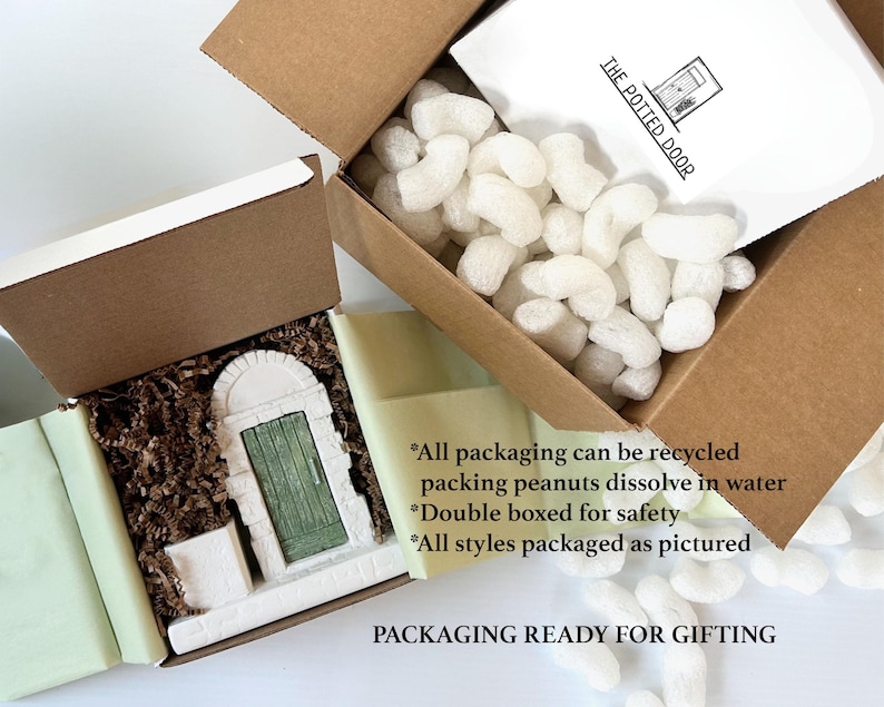 May include: Two open cardboard boxes with a decorative miniature door inside one. The door is white with a green door and is surrounded by packing materials. The other box contains packing peanuts. Text on the packaging reads "THE POTTED DOOR".