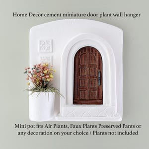 May include: White cement miniature door plant wall hanger with a brown wooden door and a small white pot holding colorful faux plants. The text on the image reads: Home Decor cement miniature door plant wall hanger. Mini pot fits Air Plants, Faux Plants Preserved Pants or any decoration on your choice.