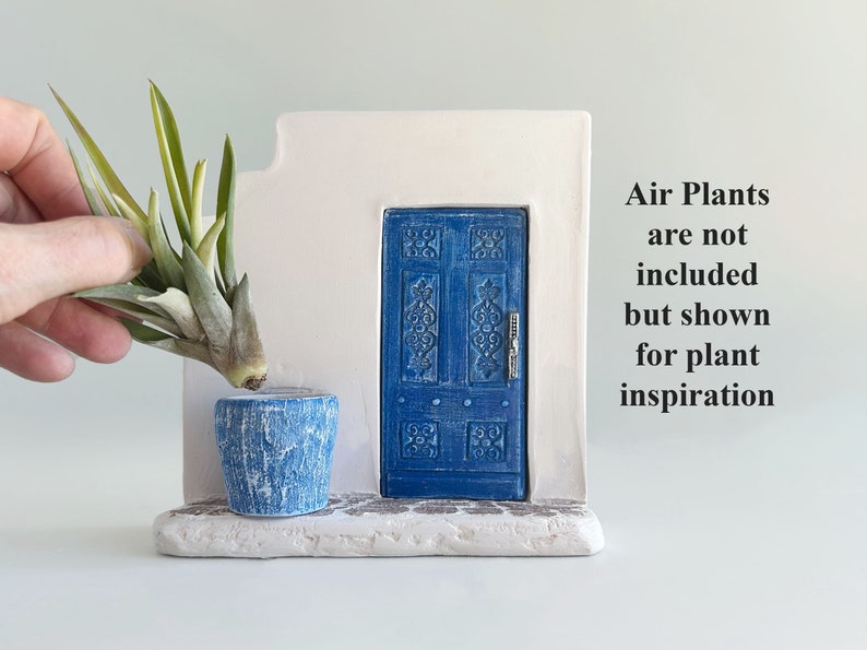 Pode incluir: Uma escultura de parede branca com uma porta azul com entalhes intrincados e um vaso azul texturizado a condizer. O texto &agrave; direita diz: Air Plants are not included but shown for plant inspiration. A base tem uma textura de pedra.
