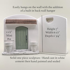 Pu&ograve; includere: Scultura in cemento bianco di un edificio in miniatura con porta verde, due piccoli vasi e tetto marrone. La scultura &egrave; alta 17,8 cm, larga 16,5 cm e profonda 4,4 cm. Il testo recita "Mini Pot".
