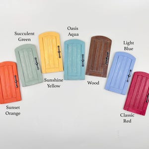 Pu&ograve; includere: Una collezione di porte delle fate in miniatura in vari colori, tra cui Arancione Tramonto, Verde Succulento, Giallo Sole, Aqua Oasis, Legno, Blu Chiaro e Rosso Classico. Ogni porta ha una maniglia decorativa ed &egrave; etichettata con il suo nome di colore.