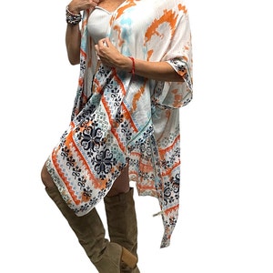 May include: White kimono with a colorful geometric pattern. The kimono has a tie closure and is made of a lightweight fabric. It is shown with a white tank top and brown knee-high boots.