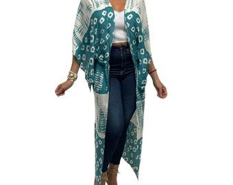 May include: A long teal blue and white patterned kimono with a geometric design. The kimono has a V-neck and long sleeves. The model is wearing the kimono over a white tank top and blue jeans.