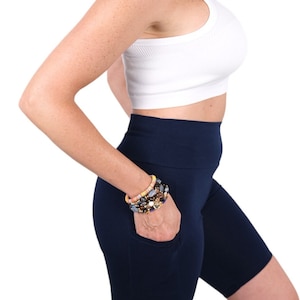 May include: A woman wearing a white tank top and navy blue high-waisted biker shorts with a pocket on the right leg.