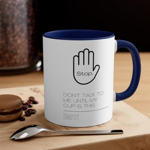 May include: White coffee mug with a blue rim and handle. The mug has a black and white graphic of a hand with the word "Stop." and the text "Don't talk to me until my cup is this EMPTY".