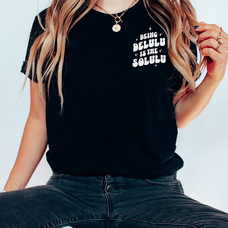 K&ouml;nnte beinhalten: Ein schwarzes T-Shirt mit wei&szlig;em Text, der "Being Delulu is the Solulu" lautet.