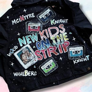 May include: Black denim jacket with hand-painted design. Features the text "New Kids On The Strip" and cassette tape illustrations. Names like McIntyre, Wahlberg, and Knight are also visible. The jacket has a button-down front.