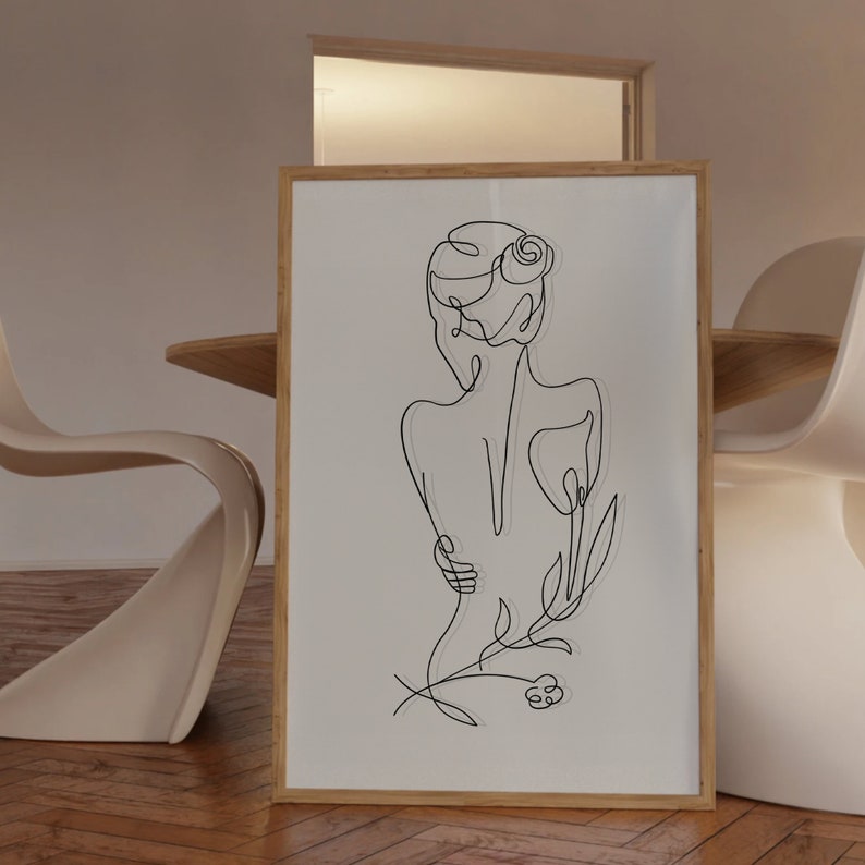 May include: A black and white line drawing of a person with a flower behind them. The drawing is framed in a light wood frame.
