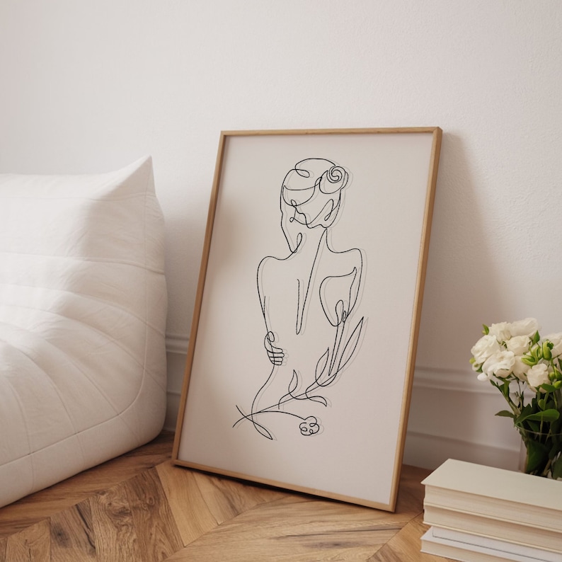 May include: A black and white line drawing of a person with a flower in their hair, framed in a light wood frame.