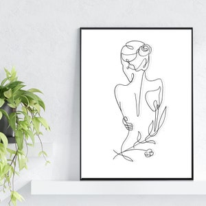 May include: Line art drawing of a person with a flower in their hair, standing with their back to the viewer. The drawing is in black and white and is framed in a black frame.