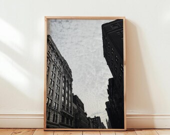 Könnte beinhalten: Schwarzweißfoto einer Stadtstraße mit hohen Gebäuden. Die Gebäude stehen auf beiden Seiten der Straße, und der Himmel ist bewölkt.
