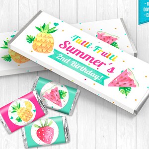 Puede incluir: Envoltorios de barra de chocolate imprimibles con un tema de frutas tropicales. Los envoltorios presentan una piña, una sandía y una fresa con el texto "Tutti-Frutti Summer's 2nd Birthday!"