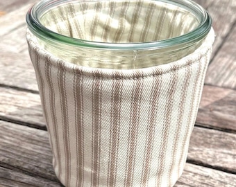 Peut inclure: Un bocal en verre transparent enveloppé dans une housse en tissu ornée d'un motif à rayures verticales beige et blanc cassé. La housse est cousue au niveau du bord supérieur et s'ajuste étroitement autour de l'extérieur du récipient cylindrique.