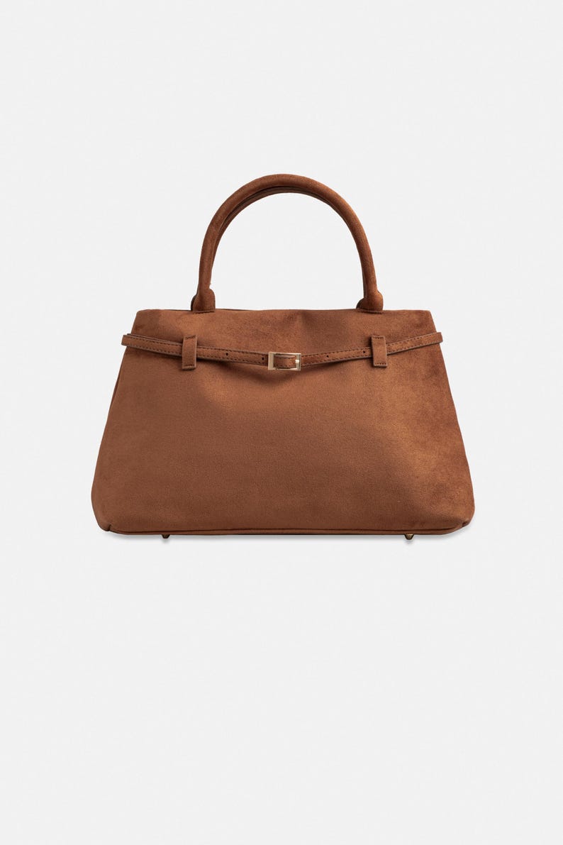Puede incluir: Un bolso marr&oacute;n con asa superior y forma rectangular. El bolso presenta un detalle de cintur&oacute;n con hebilla dorada. El bolso est&aacute; hecho de un material similar al ante.