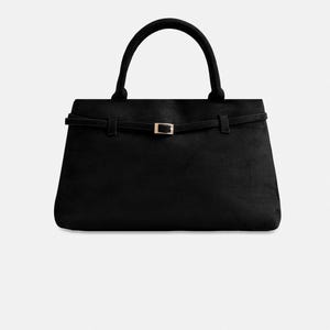Puede incluir: Bolso de mano negro con forma rectangular y asa curva. El bolso presenta una fina correa con una hebilla dorada. El bolso est&aacute; hecho de un material suave similar al ante.