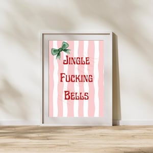 May include: A framed print with a pink and white striped background. The text "JINGLE FUCKING BELLS" is in red, with a green bow at the top. The print is in a white frame and leans against a wall.