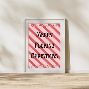 May include: A framed print with a pink and red diagonal striped background. The words "MERRY FUCKING CHRISTMAS" are in black, bold font. The top and bottom of the print are decorated with a string of Christmas lights.