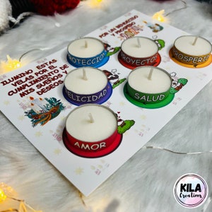 May include: A set of six tea light candles on a decorative card. Each candle sits in a colored base with a word: Protection, Projects, Prosperity, Happiness, Health, and Love. The card has text in Spanish and a logo.