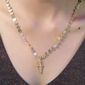 May include: A gold necklace with a dagger pendant. The necklace is made of small, round gold links.