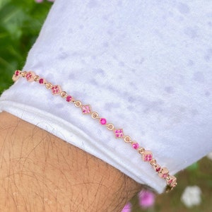 May include: A delicate gold bracelet with a chain adorned with small pink gemstones. The bracelet is on a white surface.