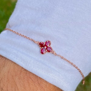 May include: A delicate rose gold bracelet with a four-leaf clover charm set with red rubies.