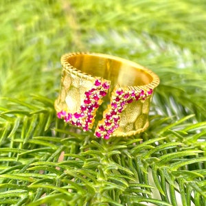 May include: Gold ring with a textured band and pink gemstones. The ring is open on one side.