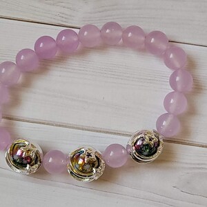 Könnte beinhalten: Ein helllila Perlenarmband. Das Armband hat runde, helllila Perlen und silberfarbene Akzentperlen mit Sternmotiven. Die Perlen sind zu einem flexiblen Band aufgereiht.