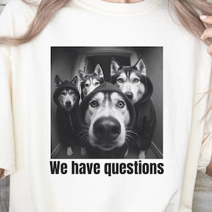May include: Ivory t-shirt with a black and white graphic of four Huskies in hoodies, and the text "We have questions". The shirt is a relaxed fit. The word "IVORY" is printed on the bottom right.