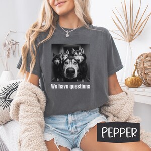 May include: Dark grey t-shirt with a graphic of four huskies wearing hoodies and the text "We have questions." The shirt is a Pepper colour.