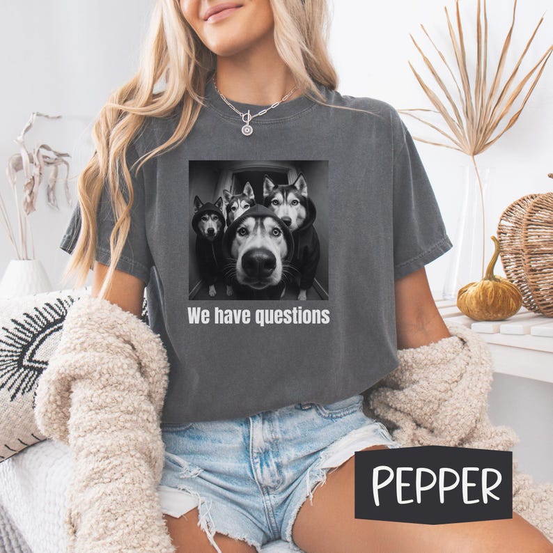 May include: Dark grey t-shirt with a graphic of four huskies wearing hoodies and the text "We have questions." The shirt is a Pepper colour.