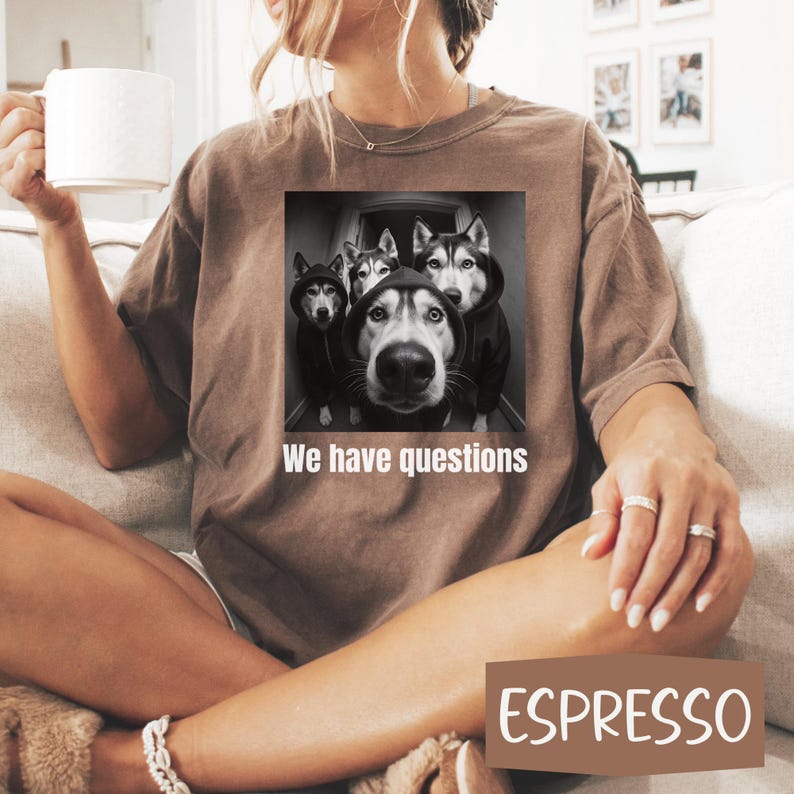 May include: Espresso-coloured t-shirt featuring a black and white image of four huskies wearing hoodies, with the text "We have questions." The shirt is a relaxed fit.