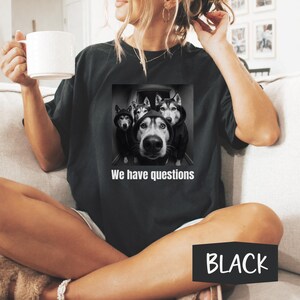 May include: Black t-shirt with a grayscale image of four Huskies in hoodies and the text "We have questions". The t-shirt is black.